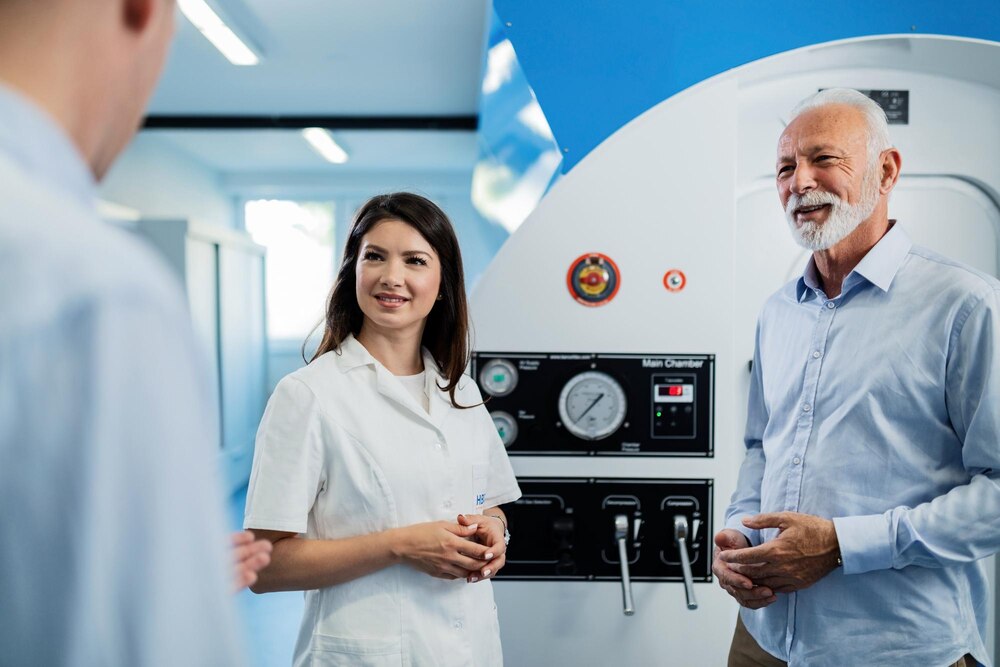 Happy senior man and female doctor talking to unrecognizable patient about experience of oxygen therapy in hyperbaric chamber