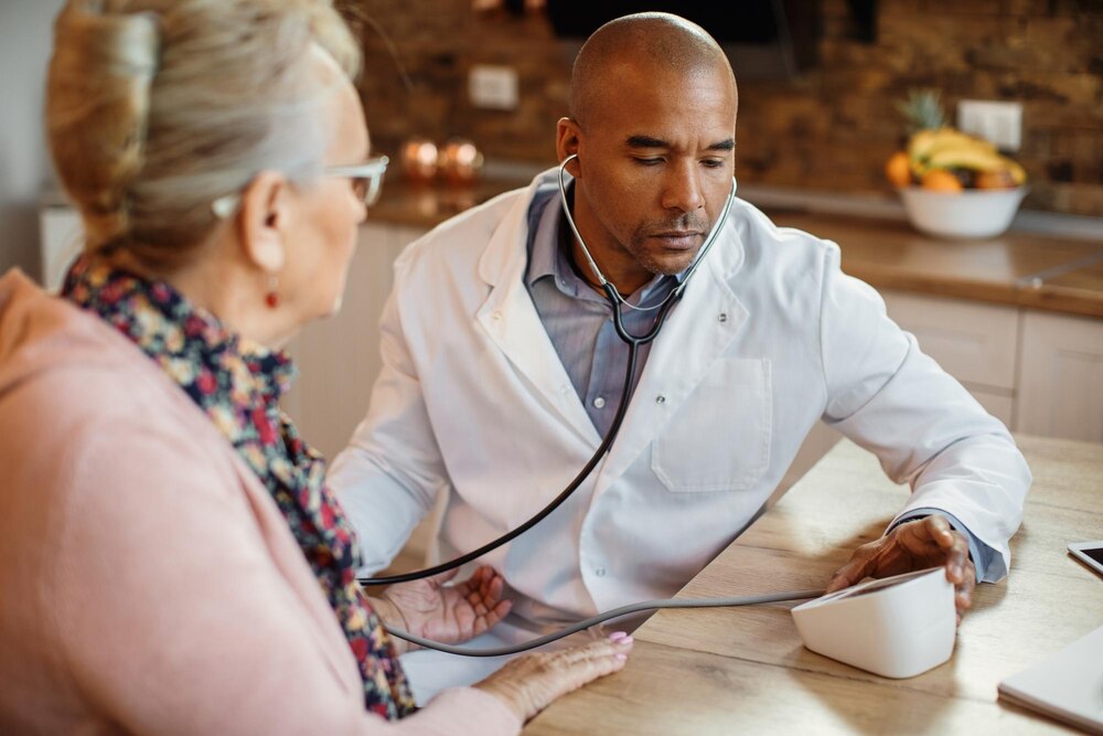 Black general practitioner measuring mature woman's blood pressure at nursing home