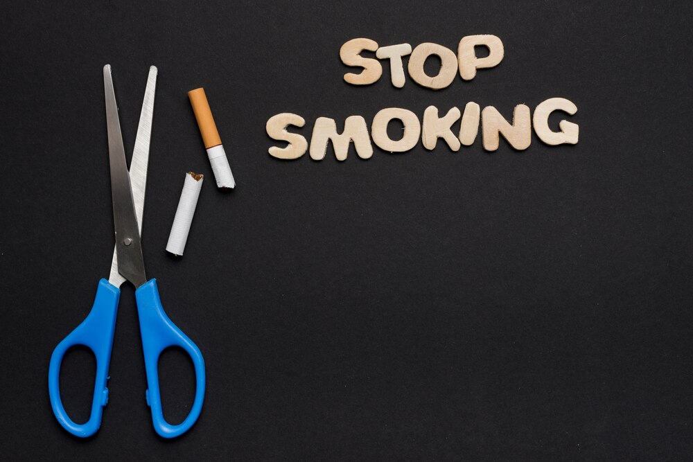 Stop smoking text with scissor and broken cigarette on black backdrop