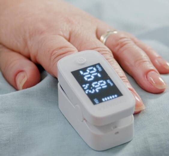 Close up of hand of aged patient with oximeter in bed. Senior person having medical tool on finger for oxygen saturation and pulse pressure measurement. Pensioner with sickness